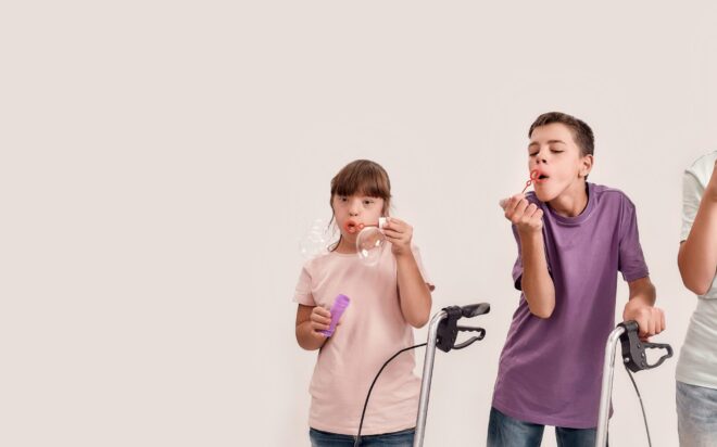 Three cheerful disabled children with Down syndrome and cerebral palsy smiling while blowing soap bubbles, standing together isolated over white background. Lifestyle of special children concept
