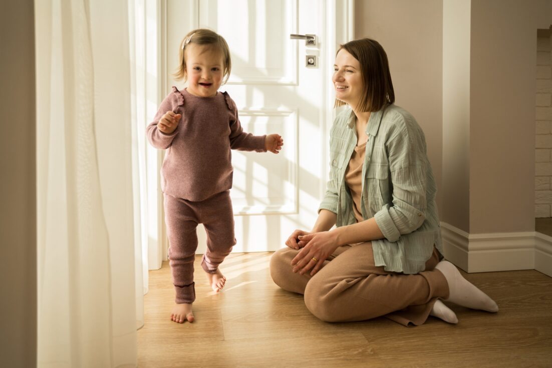 Full length view of the mother playing with her daughter with down syndrome at their apartments. People with special needs concept. Stock photo